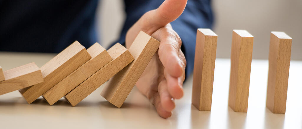 Symbolbild: Eine Hand durchbricht eine Dominokette von umfallenden Steinen